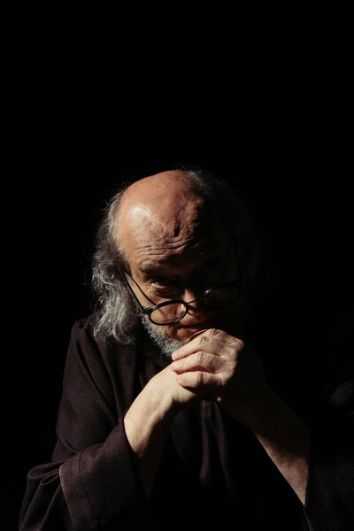 старший философ в очках и с сжатыми руками, смотрящий на камеру, изолированную на черном