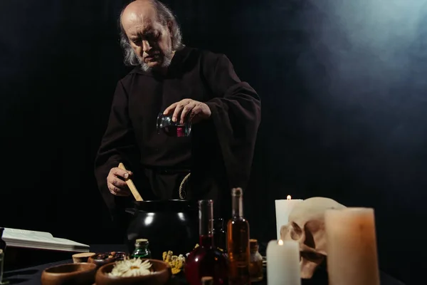 Misterioso Alquimista Añadir Ingrediente Olla Mientras Cocina Oscuro Sobre Fondo — Foto de Stock