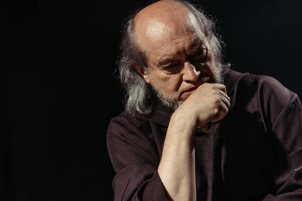 вдумчивый и серьезный священник держа руку возле подбородка изолированы на черный