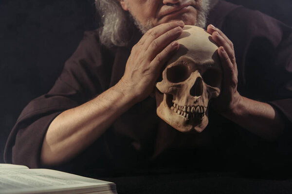 cropped view of philosopher holding skull near blurred bible isolated on black