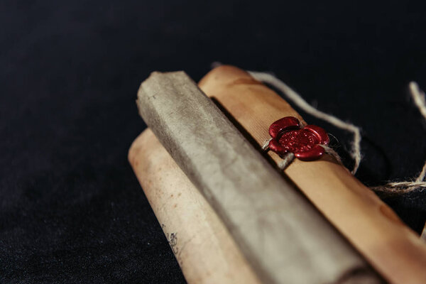 close up view of rolled manuscripts with wax seal on black background