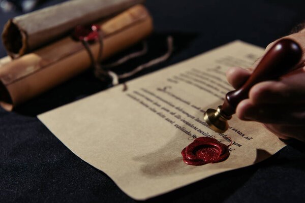 cropped view of blurred monk holding wax seal near manuscript and rolled parchments