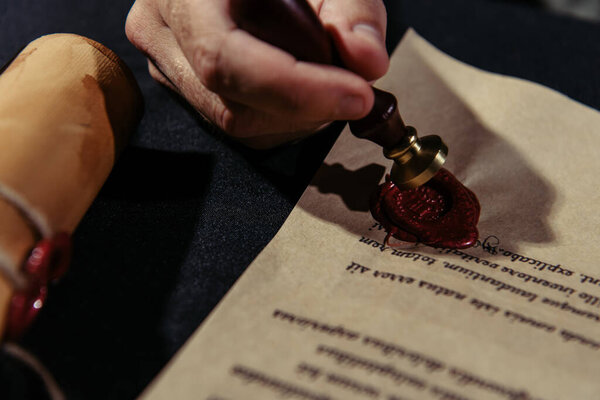 cropped view of monk approving chronicle with wax seal on black surface