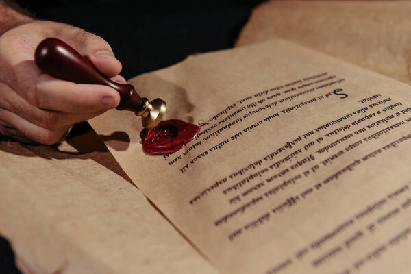 close up view of manuscript with wax seal near cropped monk isolated on black