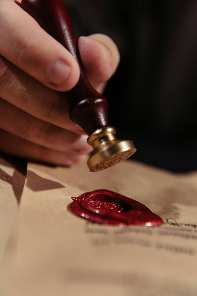 close up view of wax seal in hand of cropped priest near parchment isolated on black