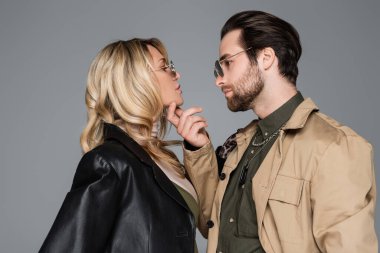 side view of bearded man in sunglasses touching face of blonde woman isolated on grey