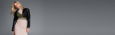 blonde woman in beige dress and black leather jacket posing isolated on grey, banner