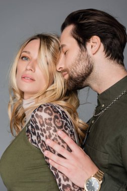 bearded man in green shirt hugging sensual blonde woman isolated on grey