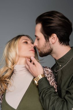 bearded man in green shirt kissing blonde girlfriend isolated on grey