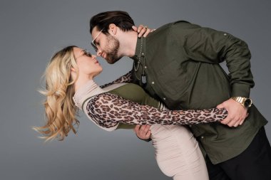 bearded man and blonde woman in sunglasses hugging isolated on grey