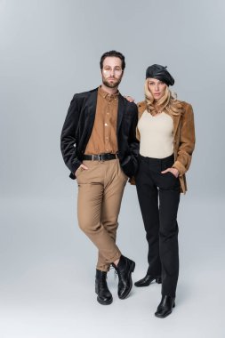 full length of blonde woman in stylish beret near bearded man in sunglasses posing on grey