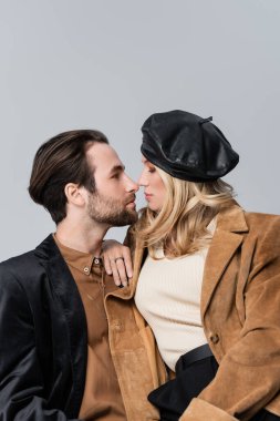 side view of blonde woman in stylish beret hugging bearded man isolated on grey