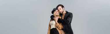 cheerful man hugging happy woman in stylish beret isolated on grey, banner