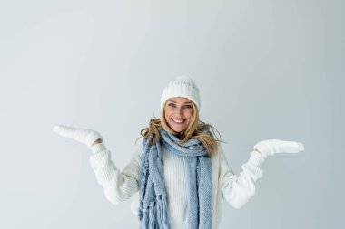 portrait of cheerful woman in winter hat and knitted scarf looking at camera isolated on grey