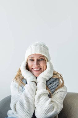 cheerful blonde woman in winter outfit and soft gloves isolated on grey