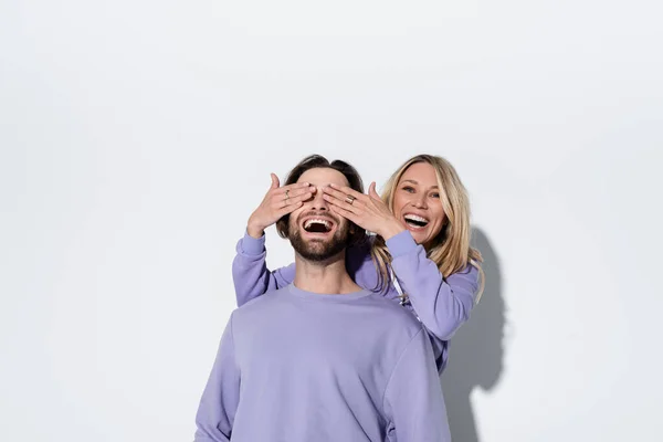 Happy Blonde Woman Covering Eyes Bearded Man Purple Sweatshirt Grey — Foto Stock