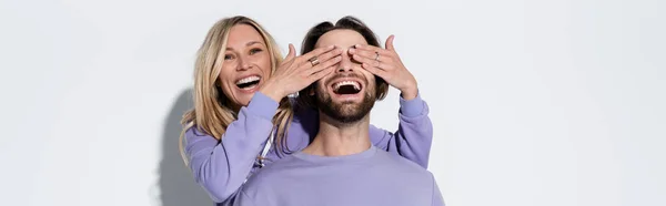 Happy Blonde Woman Covering Eyes Bearded Man Purple Sweatshirt Grey — Stockfoto