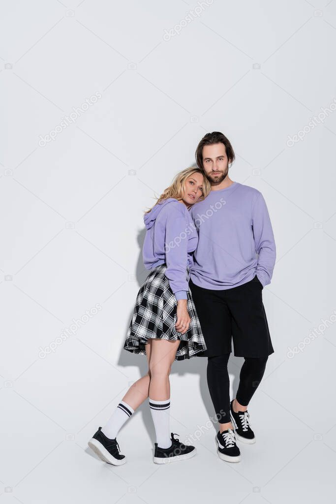 full length of bearded man posing with blonde woman in tartan skirt on grey
