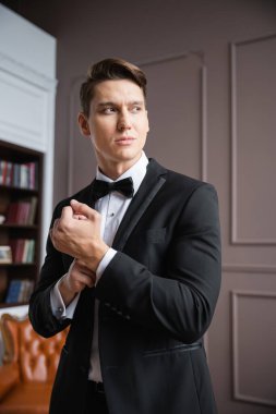 Man in formal wear adjusting sleeve of jacket at home 