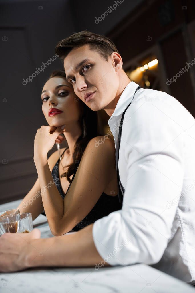 Elegant man in shirt holding glass of whiskey near girlfriend in bar 
