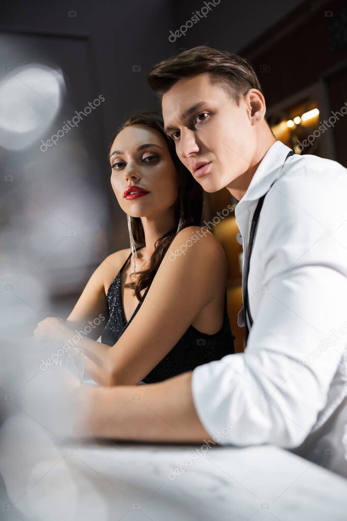Sensual woman looking at camera near boyfriend in shirt in bar 