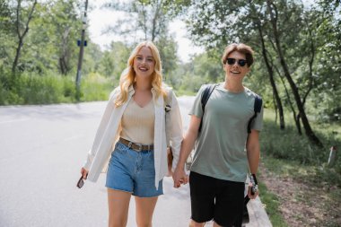 blonde woman and man in sunglasses holding hands while walking in countryside