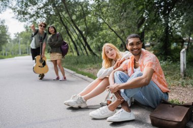 interracial friends sitting on road and looking away in countryside