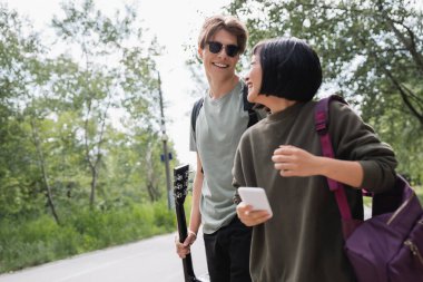 asian woman with mobile phone smiling near boyfriend in sunglasses 
