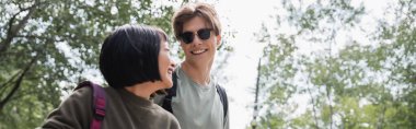 happy man in sunglasses and asian woman looking at each other on summer day, banner