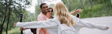 blonde woman with outstretched hands running towards interracial friends, banner