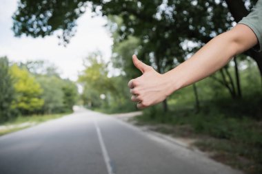 cropped view of hitchhiker with thumb up stopping car on blurred road