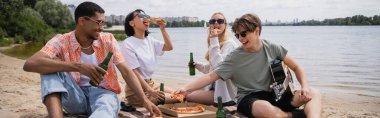 multicultural friends in sunglasses drinking beer and eating pizza on beach party, banner