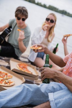 blurred multiethnic friends eating pizza and drinking beer on beach party
