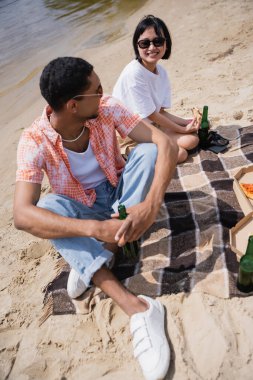 cheerful asian woman looking at african american friend during beach party