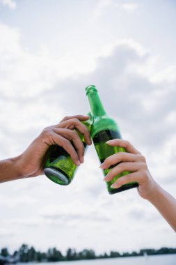 cropped view of interracial friends clinking beer bottles outdoors