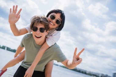 cheerful interracial couple showing victory signs while having fun near river