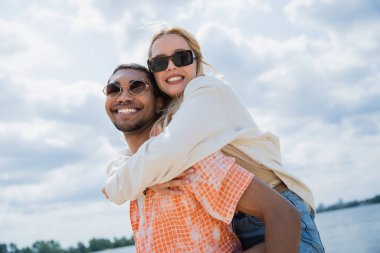 joyful african american man piggybacking smiling woman and looking at camera