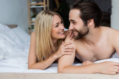 cheerful lovers looking at each other while lying on bed