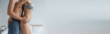 cropped view of man in pajama pants hugging woman in sexy underwear in bedroom, banner