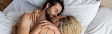 top view of brunette man and blonde woman hugging while lying on bed, banner