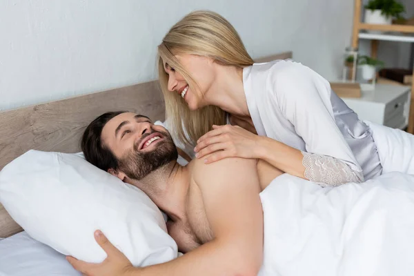 blonde woman in robe waking happy bearded man in morning