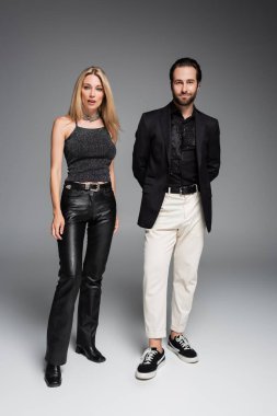 Full length of stylish couple looking at camera on grey background 