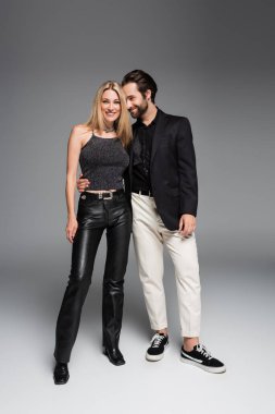 Smiling man hugging stylish girlfriend on grey background 
