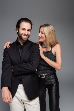 Stylish woman in leather pants hugging smiling boyfriend isolated on grey 