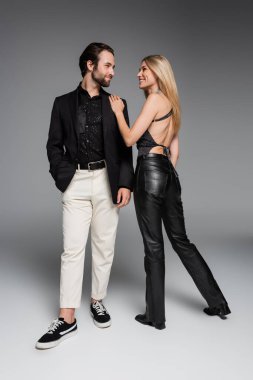 Trendy woman in leather pants hugging bearded boyfriend on grey background 