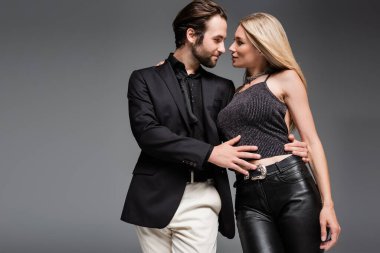 Side view of man hugging and looking at sexy girlfriend isolated on grey 