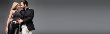 Side view of man in jacket hugging sexy blonde girlfriend isolated on grey, banner 