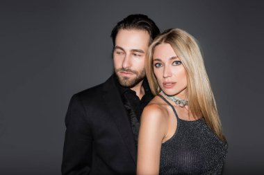 Bearded man in jacket standing near blonde girlfriend isolated on grey 