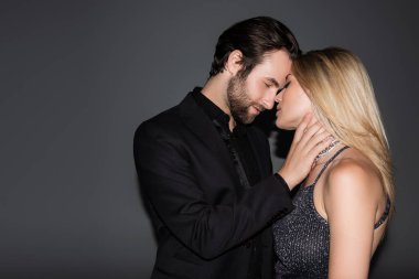 Side view of bearded man in jacket touching blonde girlfriend on grey background 