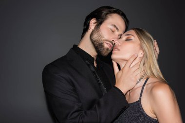 Young bearded man touching sexy blonde girlfriend on grey background 